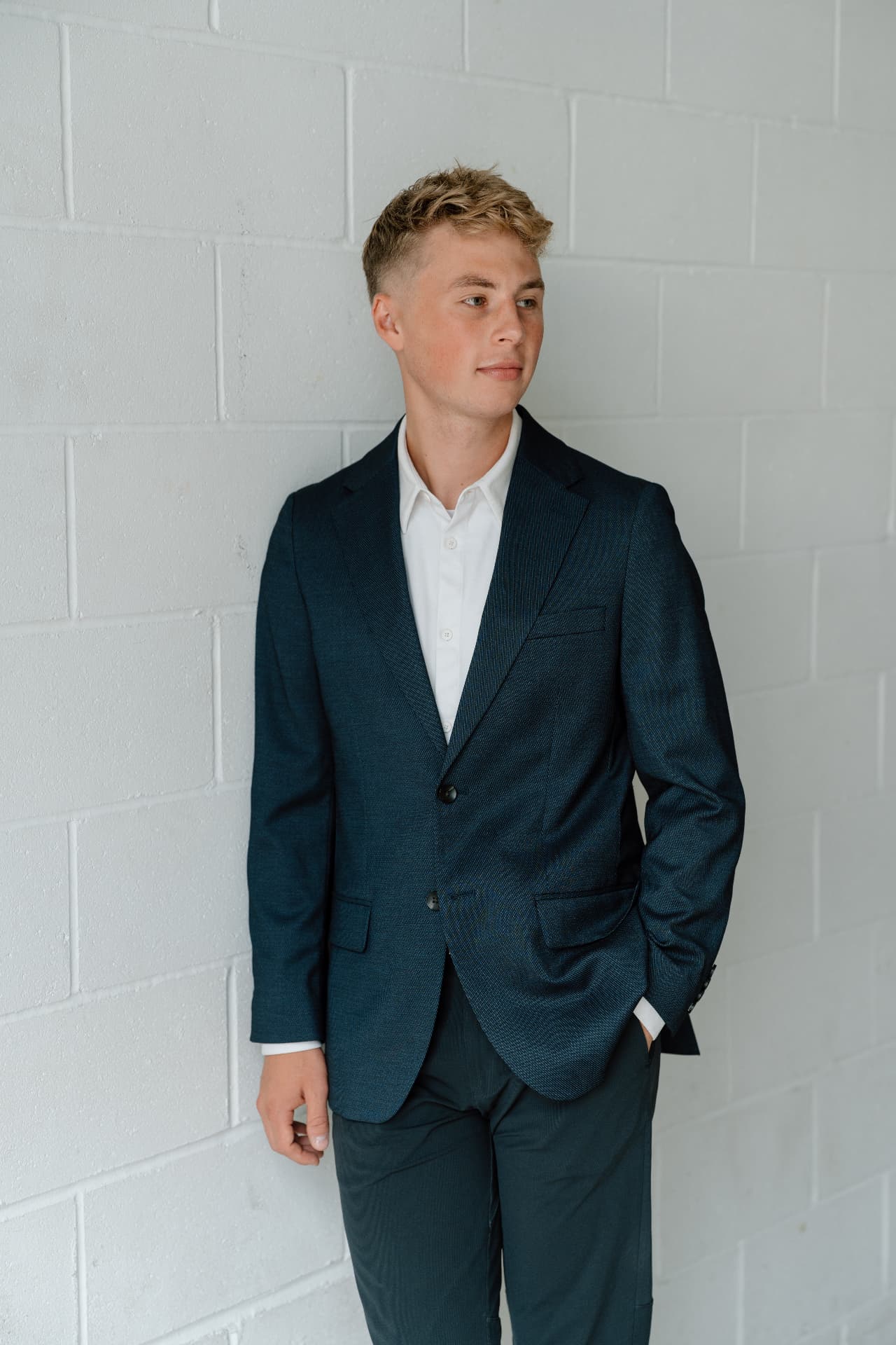 Matt Schertzer in a navy blazer leaning against a white brick wall, looking thoughtfully to the side.