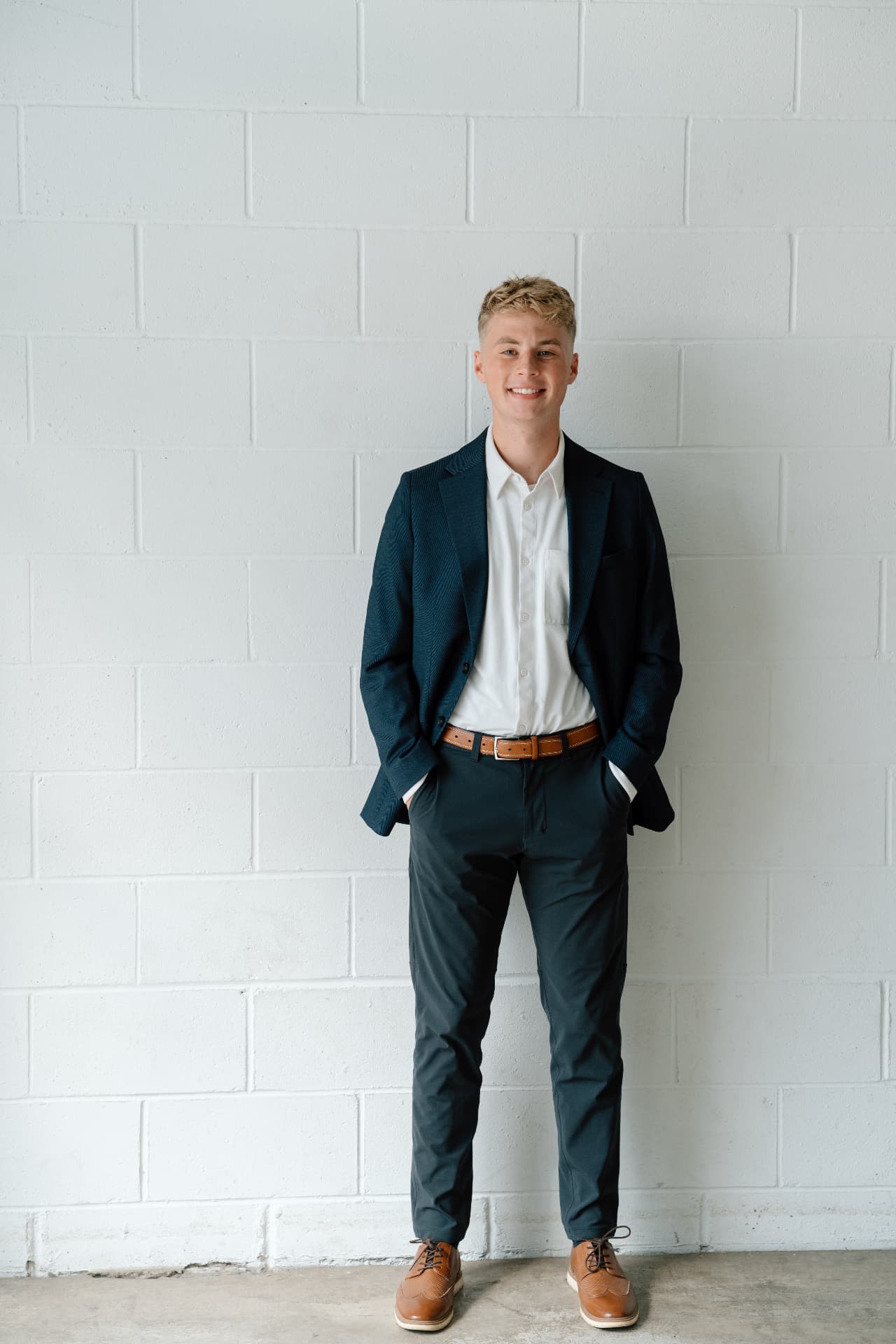 Matt Schertzer smiling in a navy blazer, standing against a white brick wall.